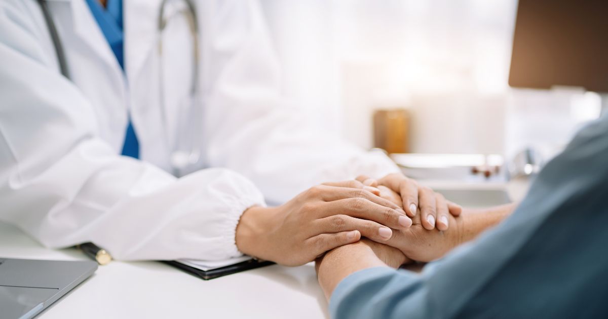 medical professional hold the hand of a patient at a desk.