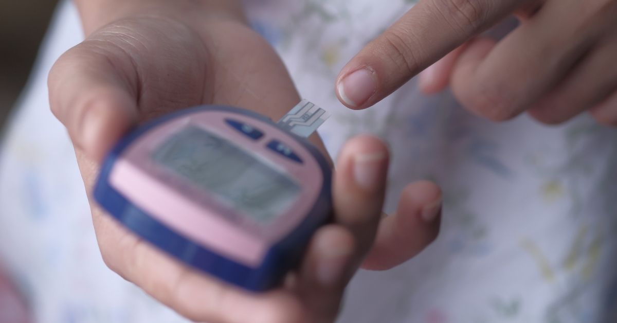A photo showing a diabetic testing their blood with a finger prick. The picture is a close up so only the hands are visible.
