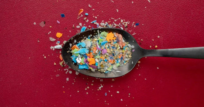 Dessert spoon on red background with multi colored sprinkles of plastic pieces