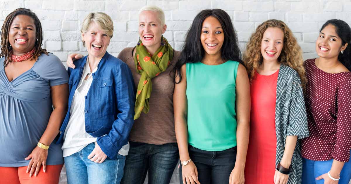 Line up of six women of various ages, standing up and laughing