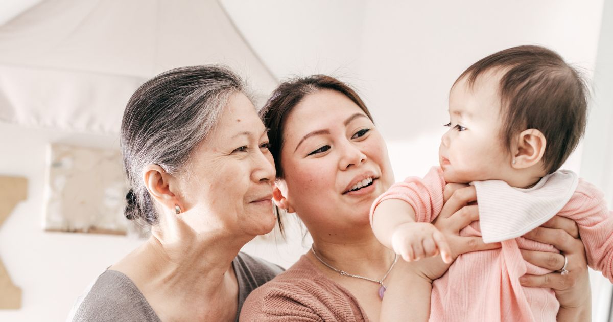 A baby being held by their mother, with grandmother standing behind the mother