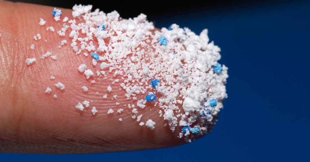 White and blue microplastics on the end of a finger