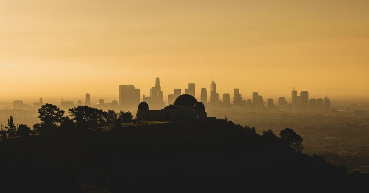 A photo showing downtown Los Angeles, with Griffith Observatory in the foreground. The air is looks brownish orange as though there is a wildfire.