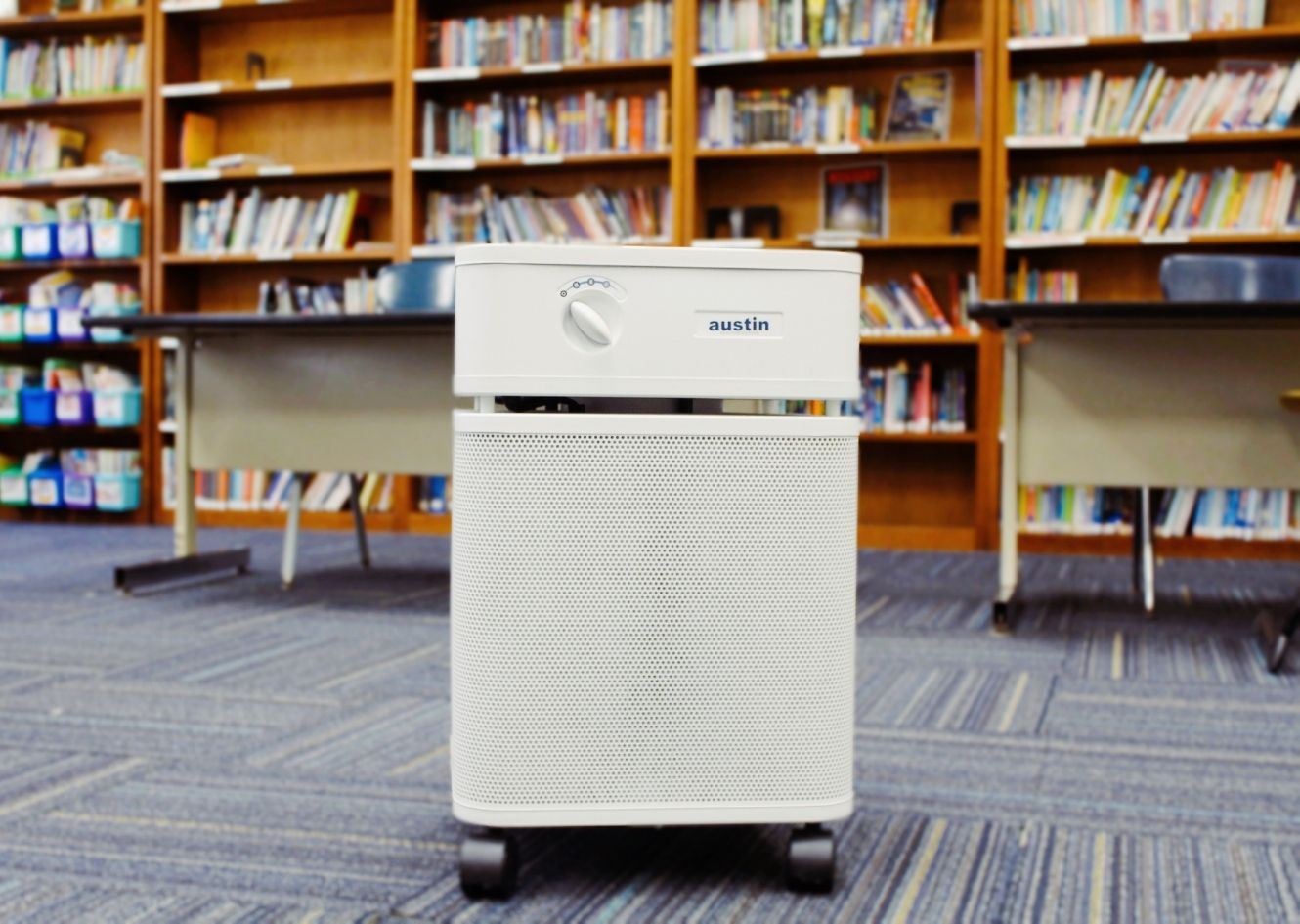 Air purifier on a carpeted floor with bookshelves in the background