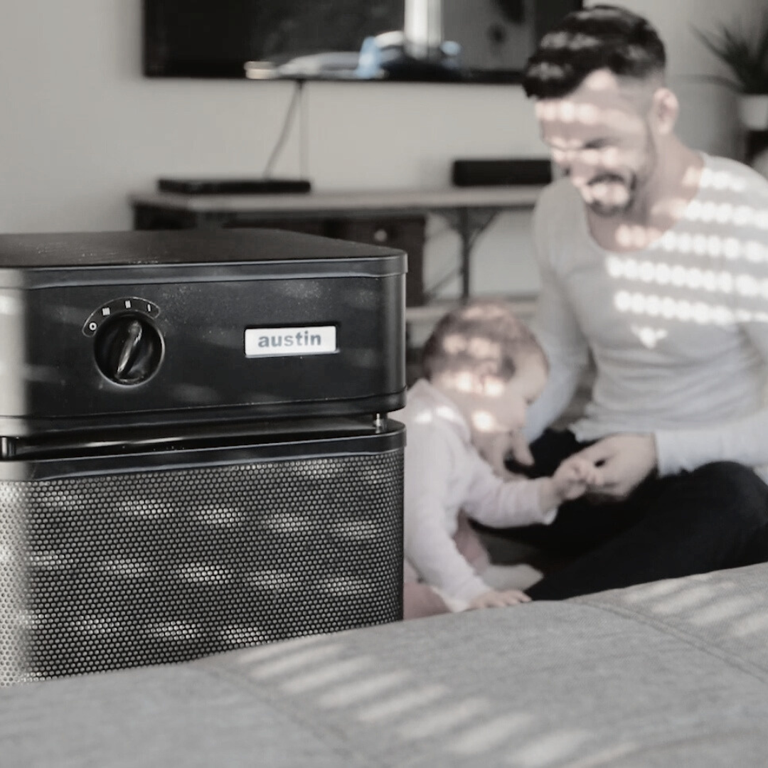 Man and young child interacting with an Austin Air purifier nearby.