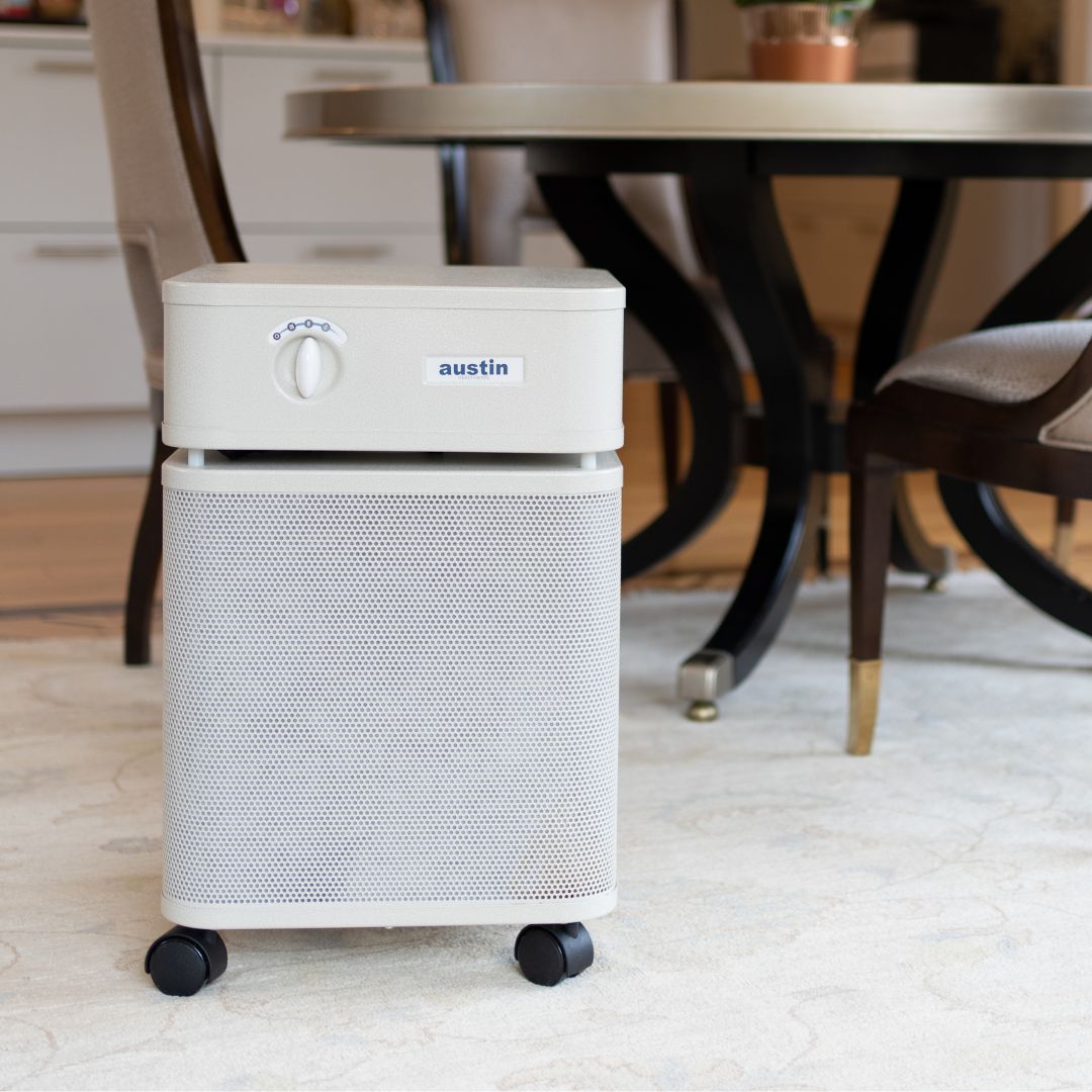 Austin Air HealthMate air purifier on a carpeted floor in a room with furniture.