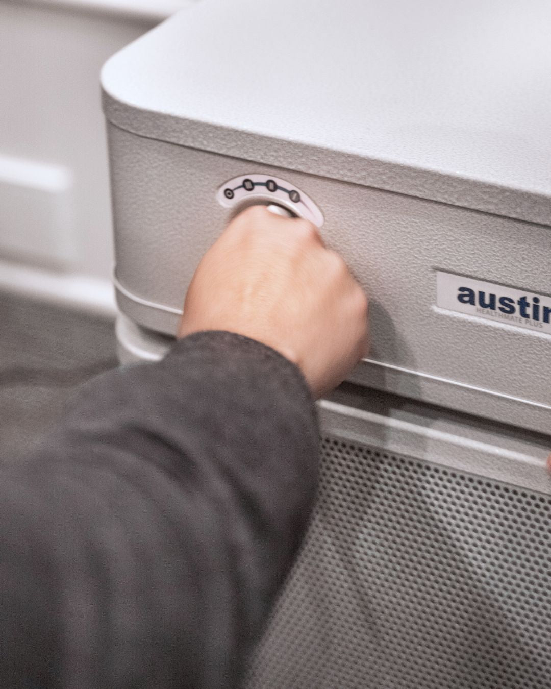 an austin air unit with a hand adjusting the knobs showing it has no wifi connection and is made of solid sturdy steel