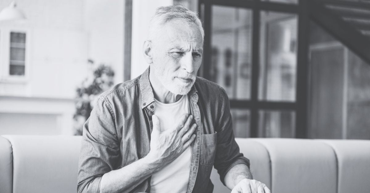 Middle aged man sitting on sofa holding his chest