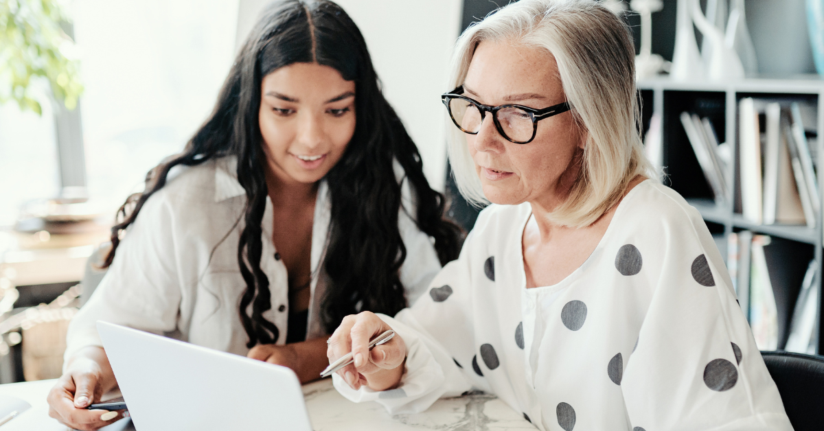 Two women sitting at a desk looking at a laptop