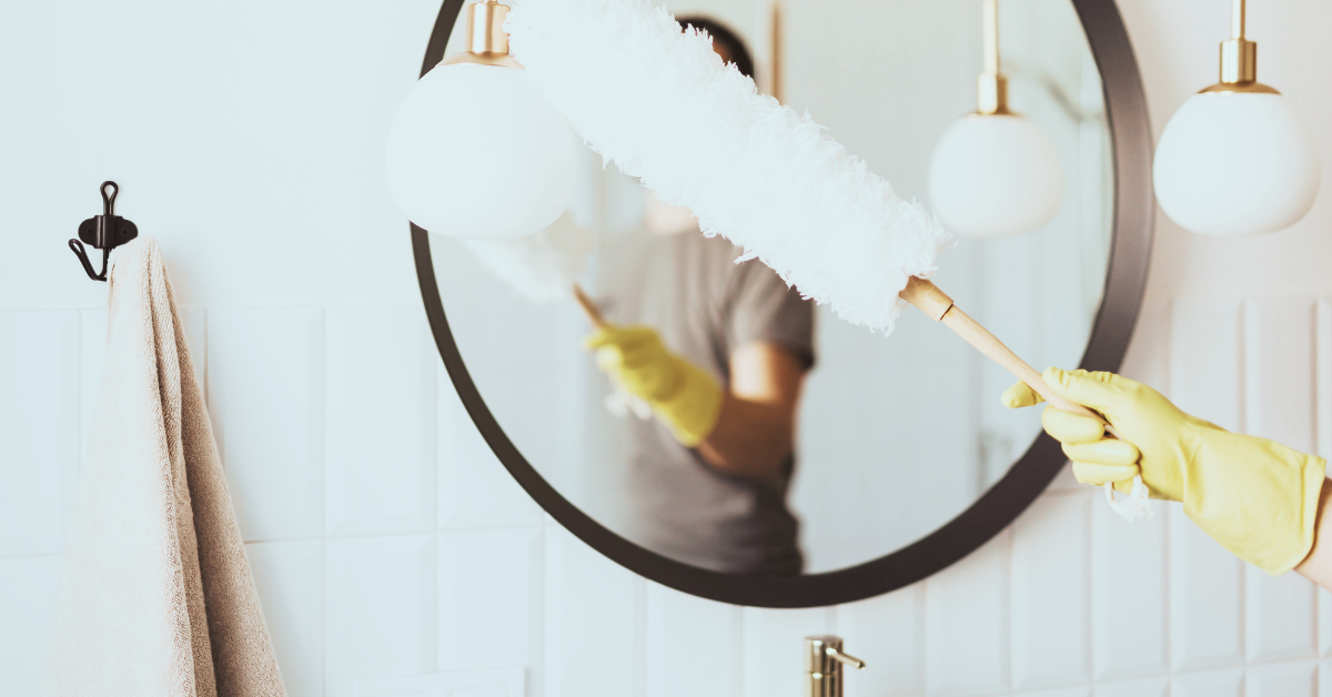 Person wearing yellow rubber gloves is using a duster to clean a round mirror