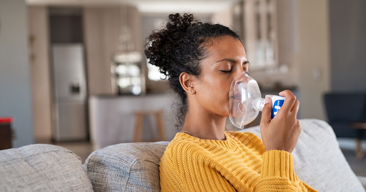 Woman sitting on sofa using a nebulizer.