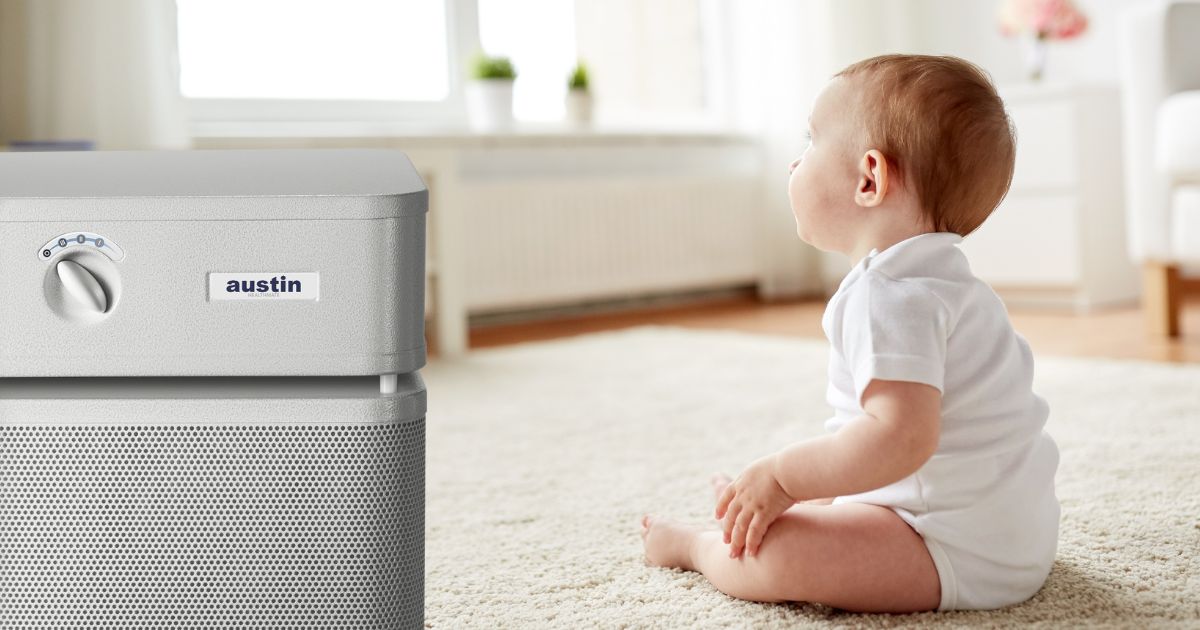 Baby sitting on the floor next to an Austin Air purifier