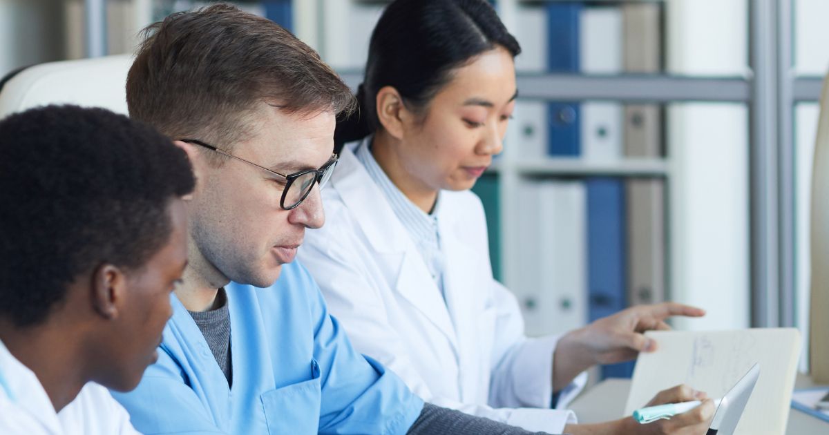 Two men and one woman medical professionals sitting at a desk reading documents 