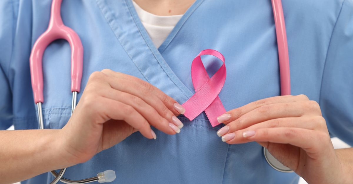 A close up photo of a woman with manicured nails in medical scrubs, wearing a pink stethoscope,affixing a pink ribbon for breast cancer awareness to her chest.