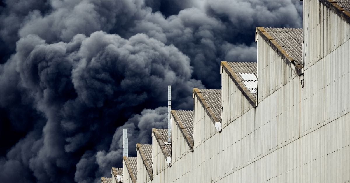 A photo showing an outside view of a large factory with huge plumes of black smoke billowing out of it.