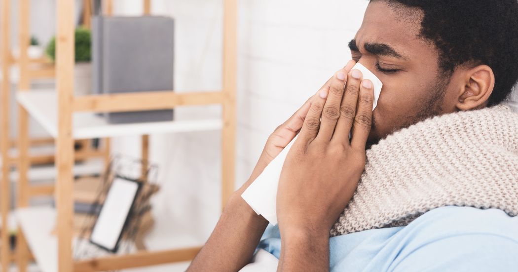 Man sitting down wrapped in blanket and blowing his nose