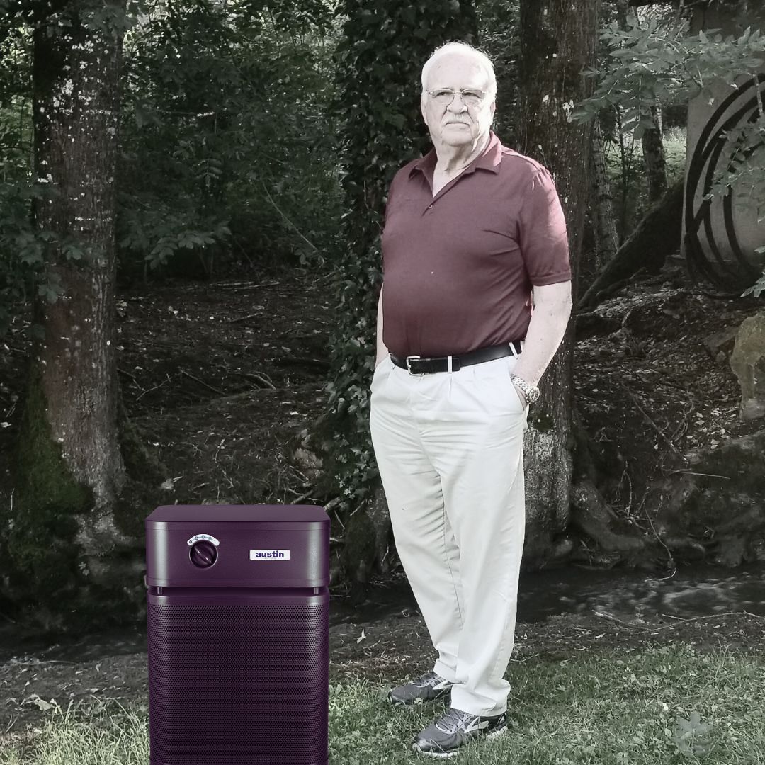 Man standing next to a black Austin Air purifier in a wooded area