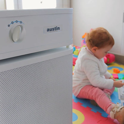 Child playing on a colorful mat next to an Austin air purifier