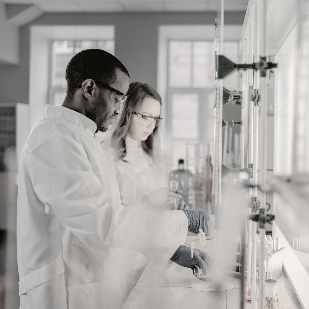 Two scientists in a laboratory setting, wearing white lab coats and gloves.