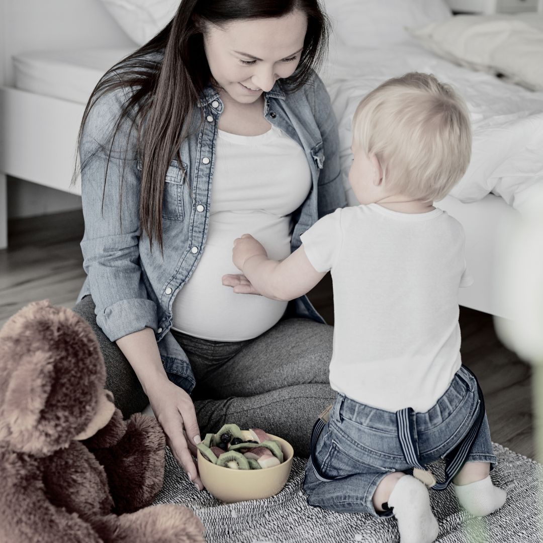 Pregnant woman sitting on the floor with a toddler and toys