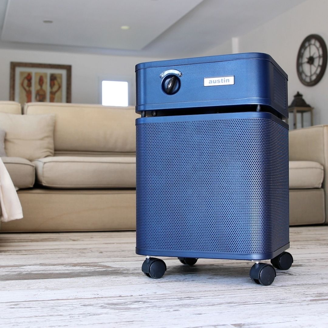 Austin air healthmate plus blue air purifier on a wooden floor with a living room background