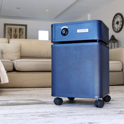 Austin air healthmate plus blue air purifier on a wooden floor with a living room background