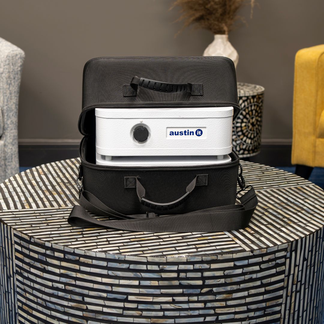 Austin air "it" air purifier with 'austin' branding in a black carrying case on a patterned table.
