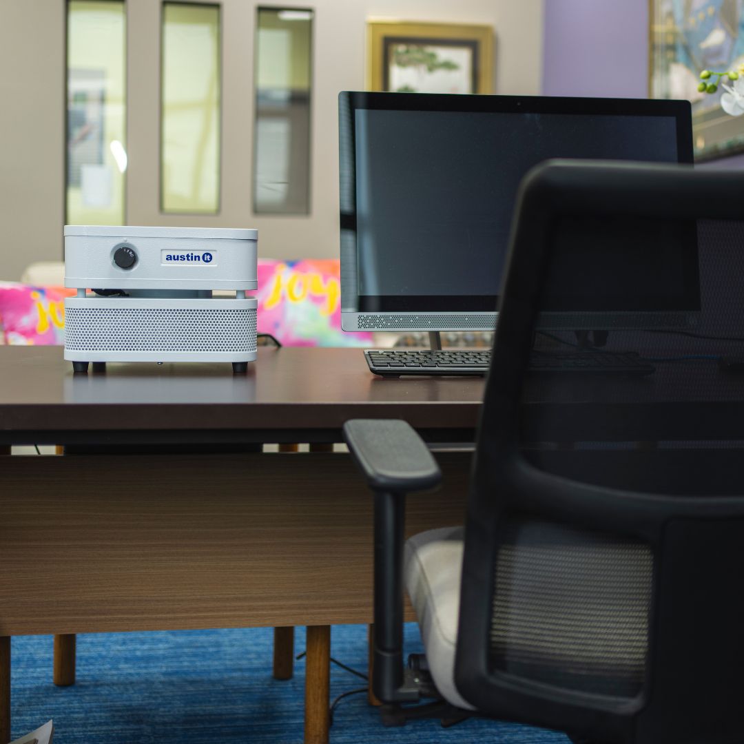 Austin air "it" on an office desk with computer setup, chair, and colorful decorations in the background