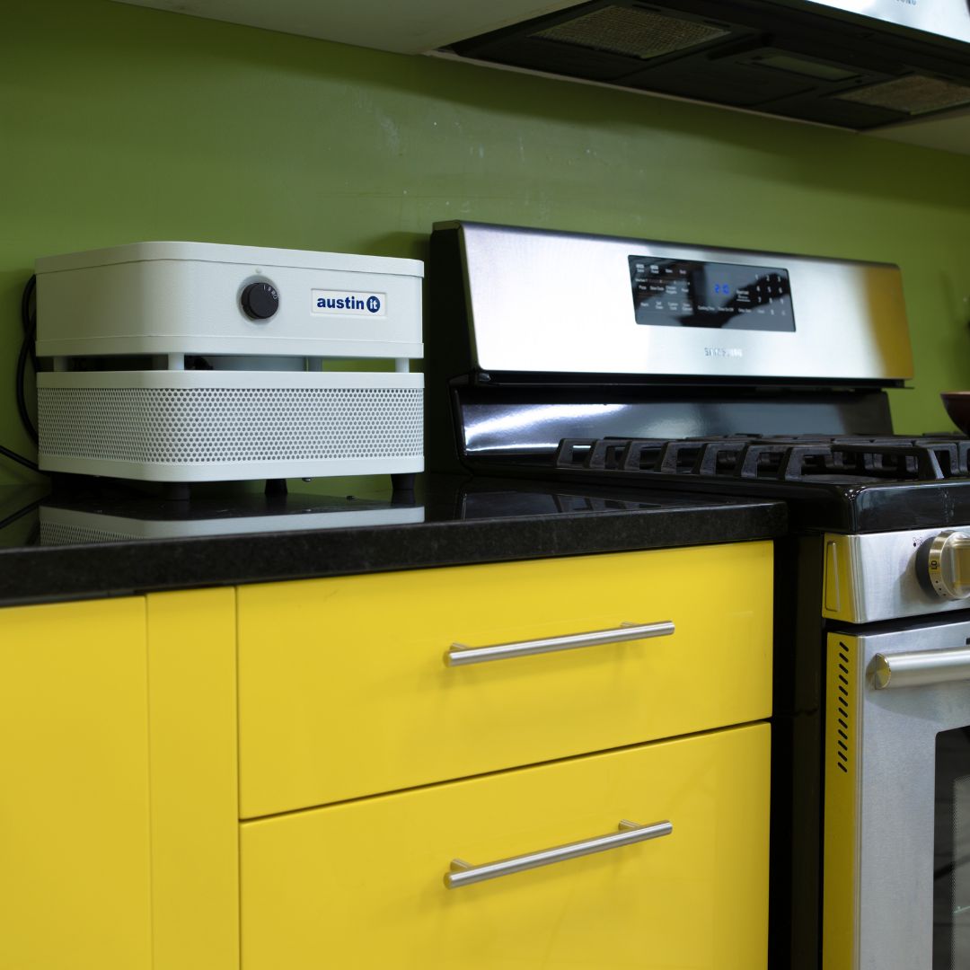 Kitchen with yellow cabinets, black countertop, and stainless steel appliances including a coffee machine and oven with the Austin air "it" on the counter